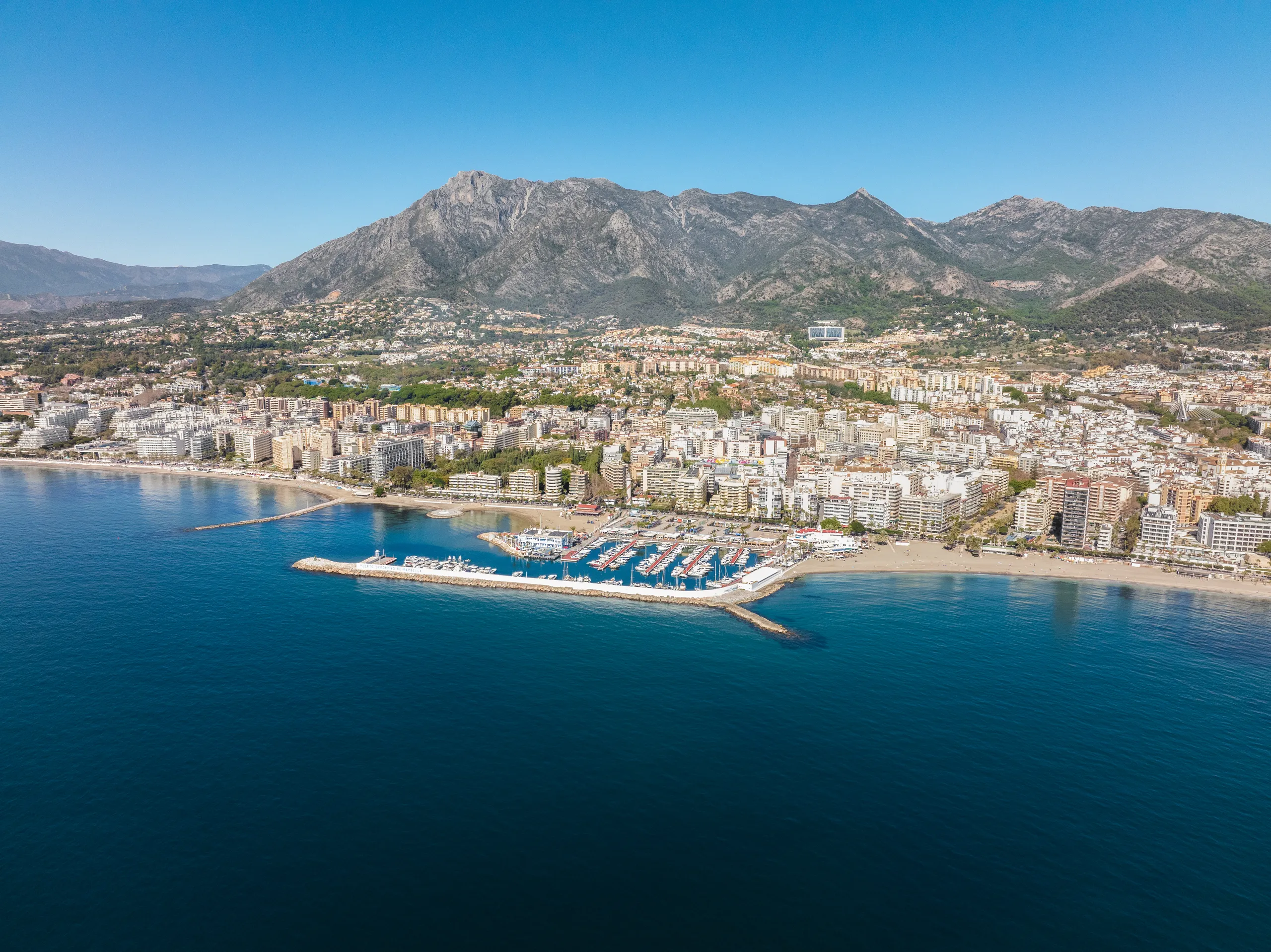 Vista aérea de Marbella: el puerto deportivo, la playa y la ciudad, con La Concha y Sierra Blanca al fondo.